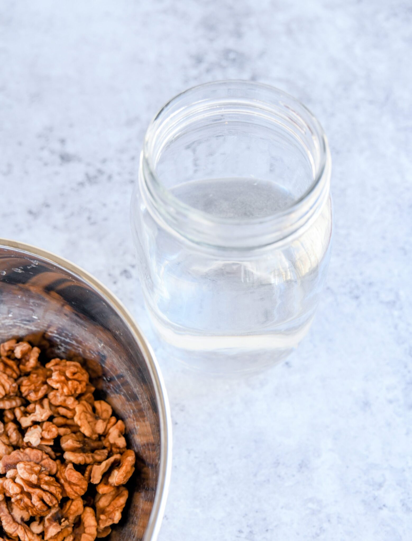 walnuts soaking in a metal bowl with water next to a glass jar with water