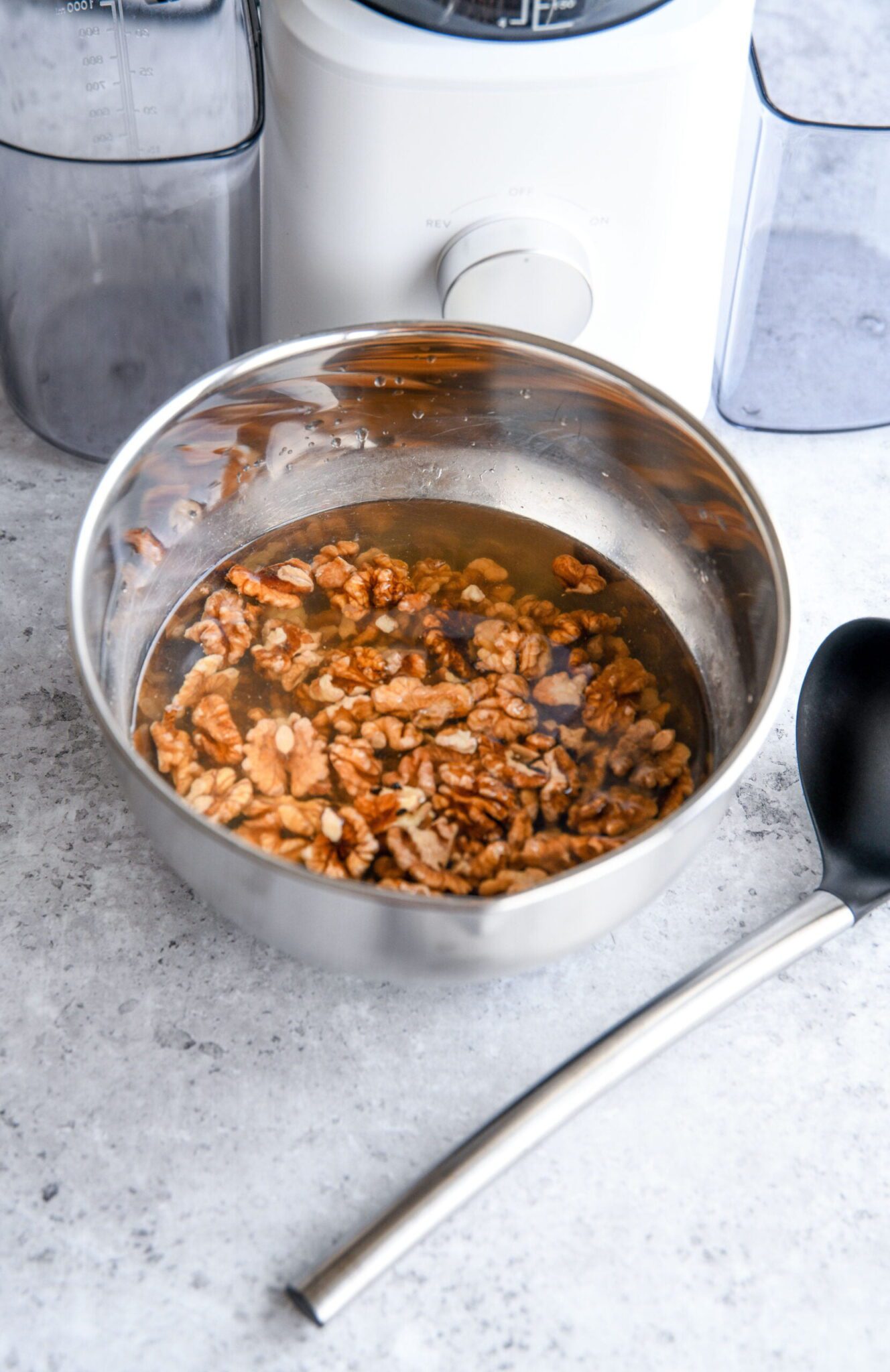walnuts soaking in a metal bowl with water next to a ladle