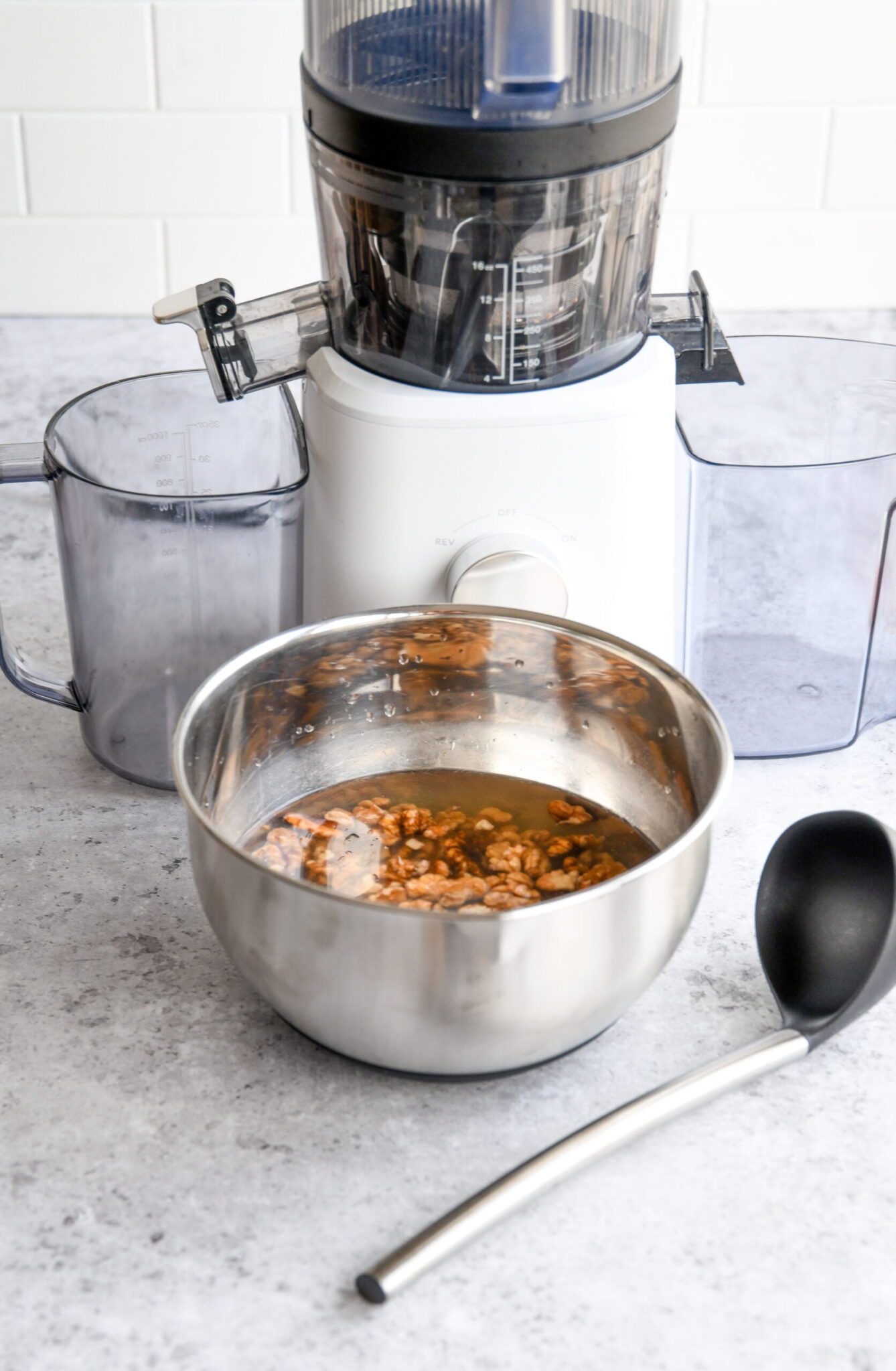 walnuts soaking in a metal bowl with water next to the Nama J2 juicer