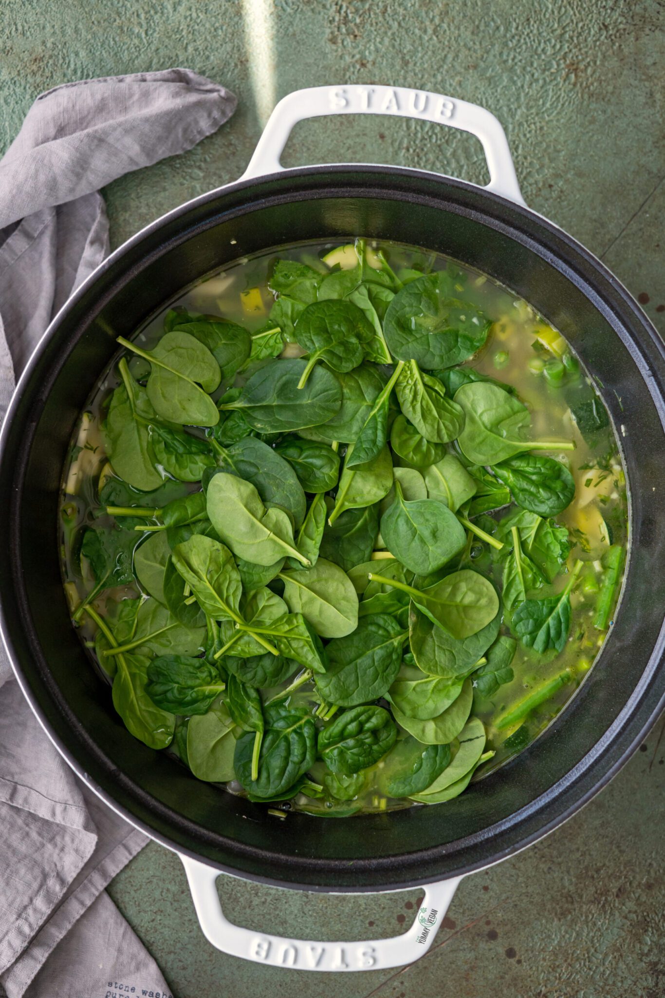 Green Minestrone Soup in a pot cooking with fresh spinach being added