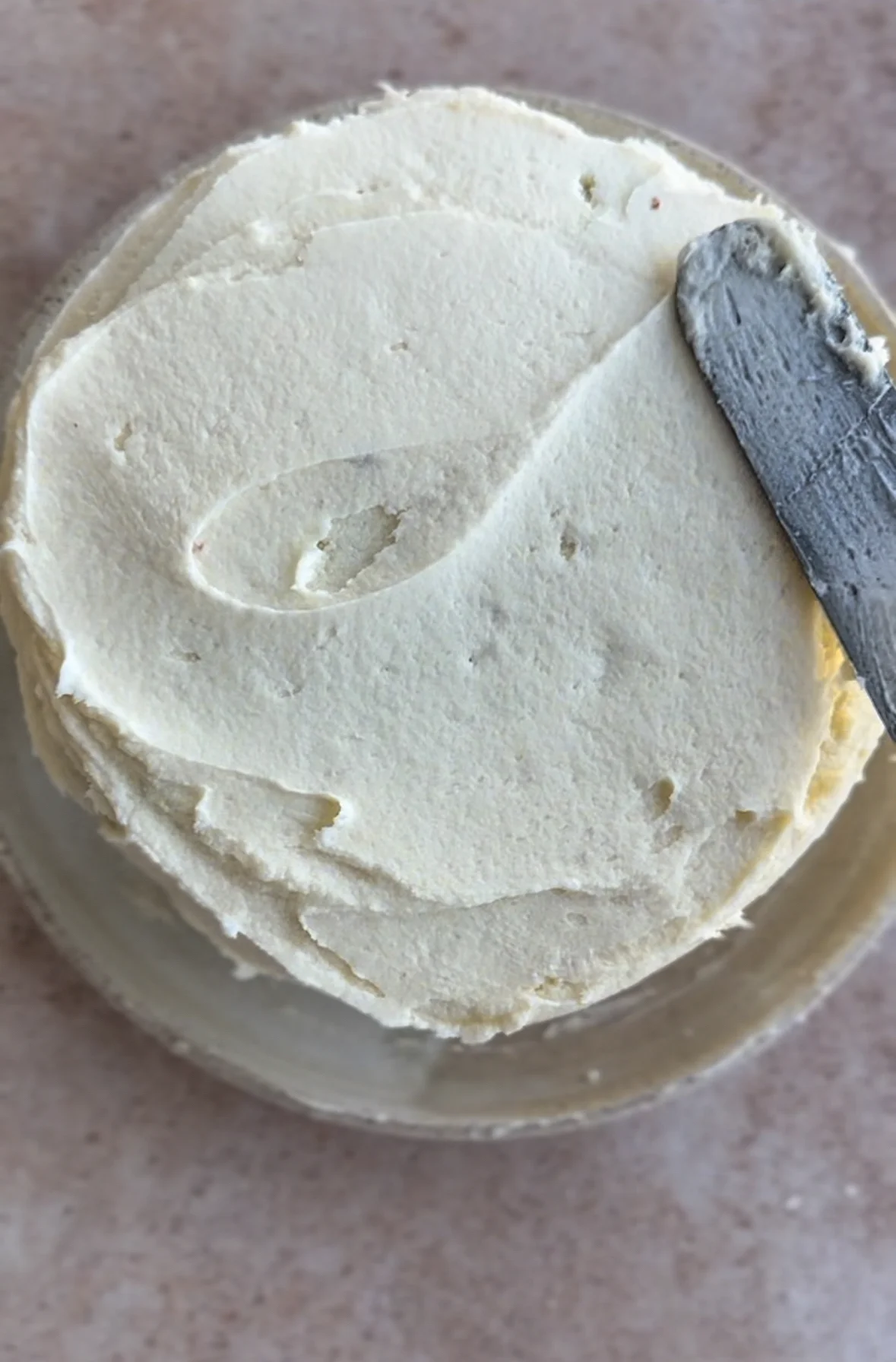 overhead shot of vegan cream cheese frosting being added to a cake layer