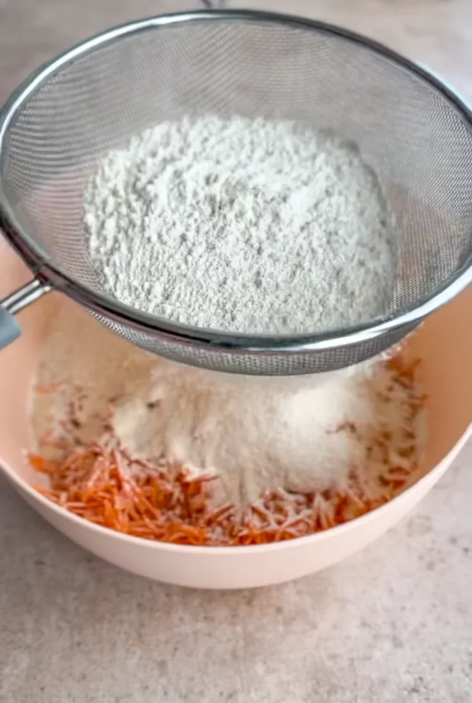 flour being sifted into the bowl with the other cake batter ingredients