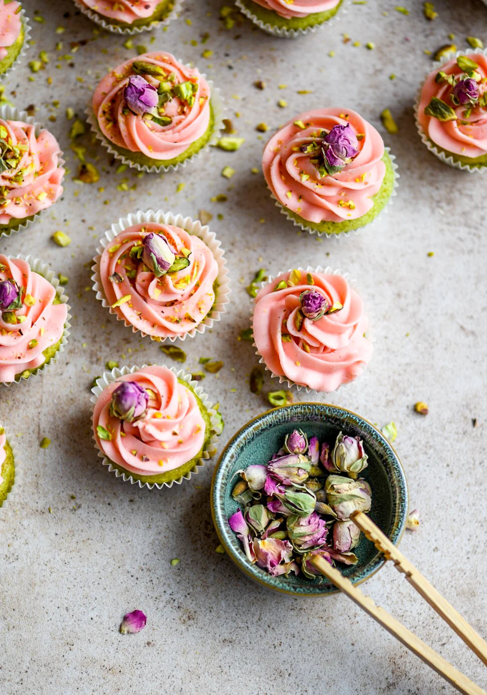 green mini cupcakes with pink buttercream topped with chopped pistachios and dried rose buds